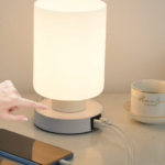 a TV Lamp on the table with a USB charger charging a phone and a cup